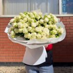 Великий букет білих троянд на фоні цегляної стіни.
