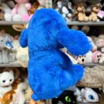Синя іграшка-собака на фоні інших м'яких іграшок.